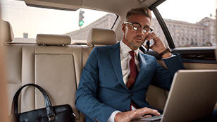 man in a suit talking on a cell phone in the back seat of a car